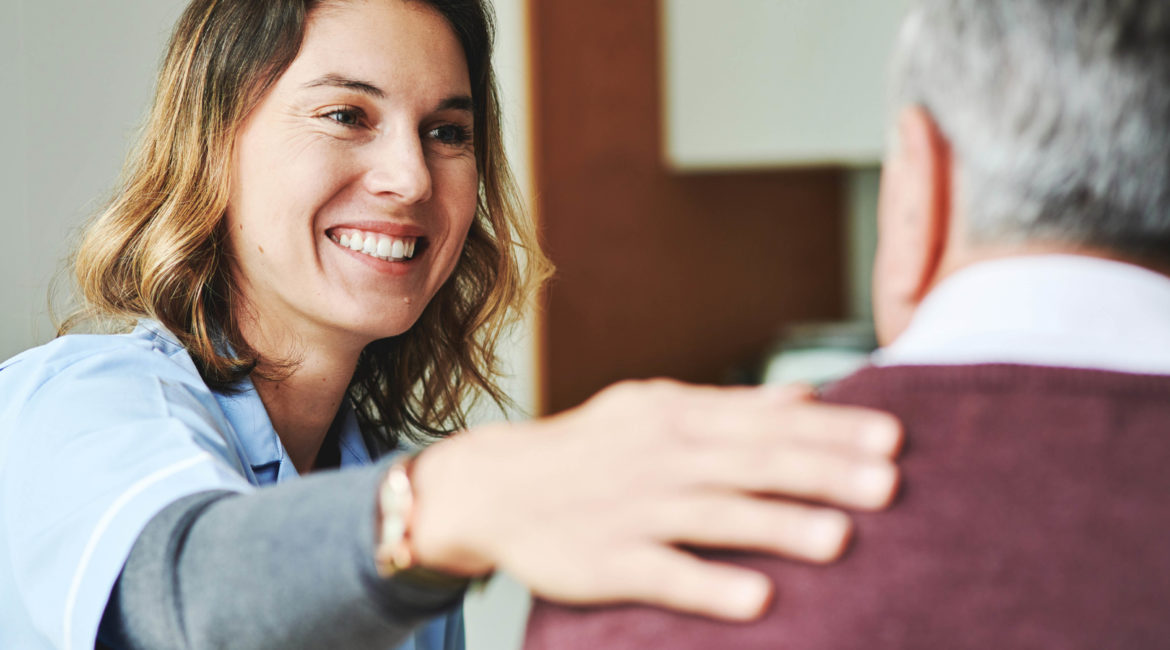 Female nurse patting elderly male patient on the shoulder while smiling