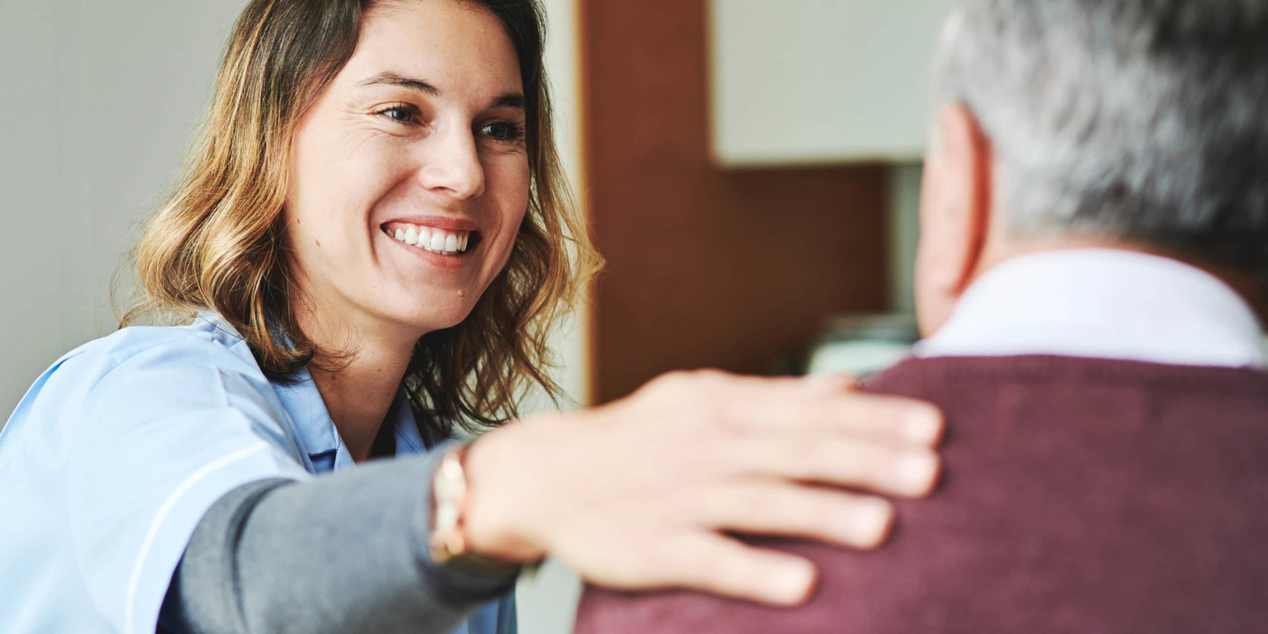 Female nurse patting elderly male patient on the shoulder while smiling